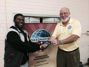 Student Samiel Remy accepts his Best Table-Topics ribbon from Homestead Toastmasters Club President Richard Erschik.