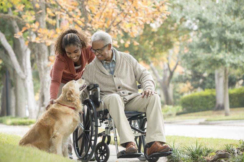 man in wheelchair with caregiver and dog